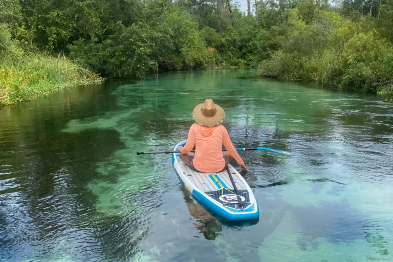 Mulher de chapéu fazendo stand up paddle em rio cristalino de spring na Flórida